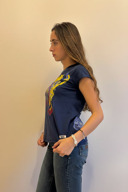 A woman wearing our Cats tee, a navy blue graphic t-shirt with a colorful abstract cat print and dark wash jeans, shown from a side profile against a plain beige wall.