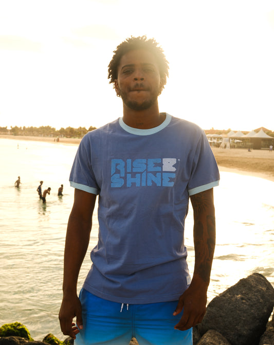 Man wearing the signature blue Rise & Shine t-shirt on a pier by the beach in Sal, Cabo Verde.