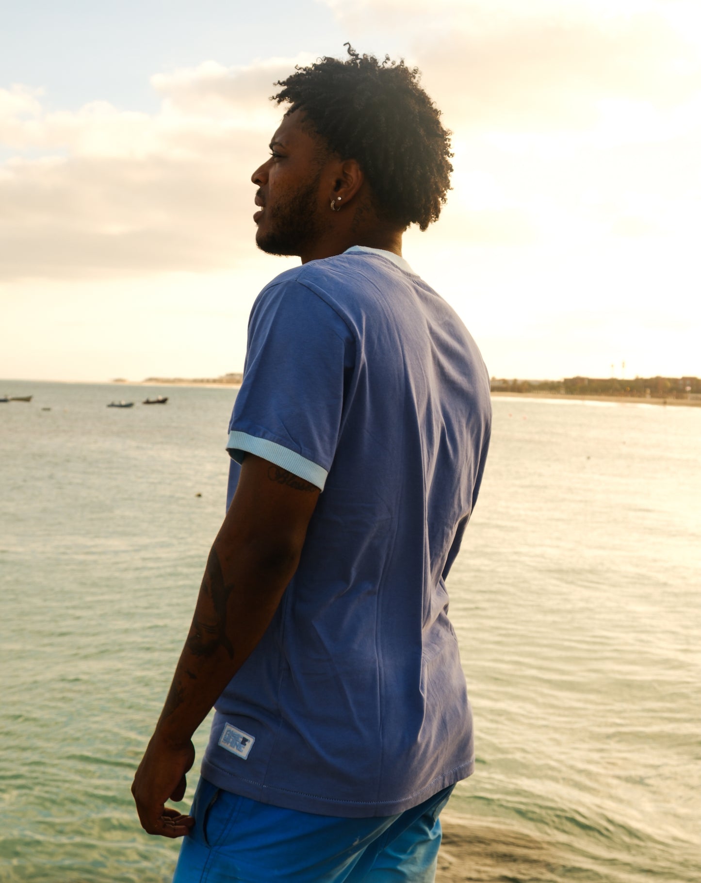 Man wearing the signature blue Rise & Shine t-shirt on a pier by the beach in Sal, Cabo Verde.