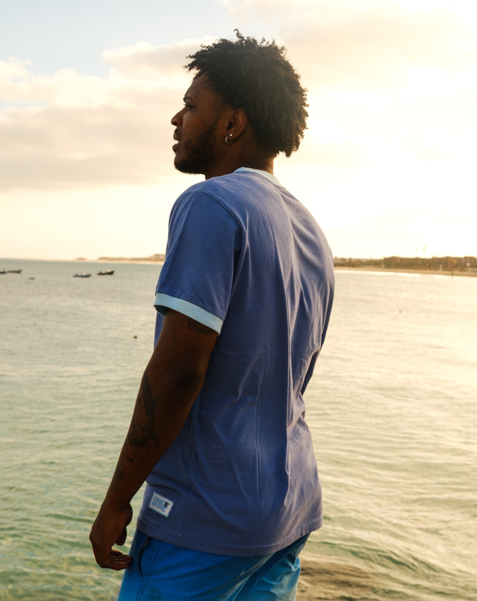 Man wearing the signature blue Rise & Shine t-shirt on a pier by the beach in Sal, Cabo Verde.